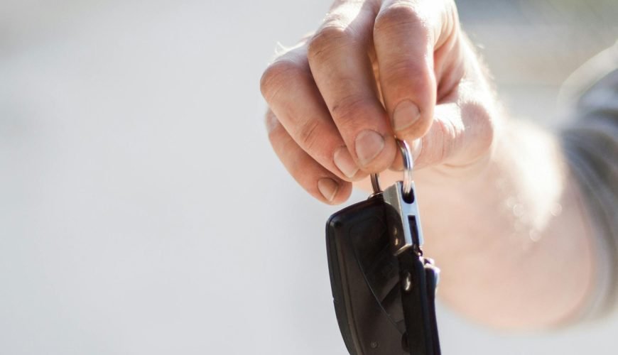 Close-up of a hand handing over car keys, signifying purchase or rental.